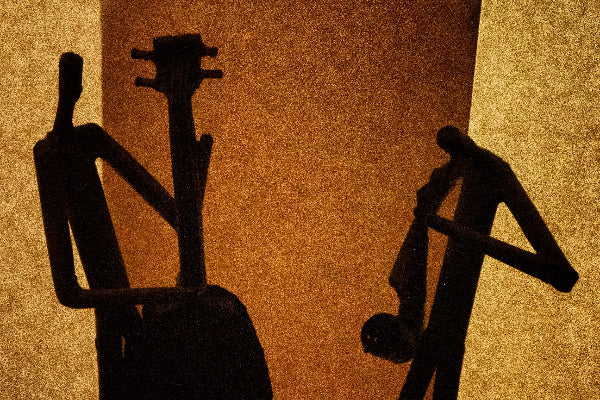 Silhouette of two figures playing stringed instruments against a brown background